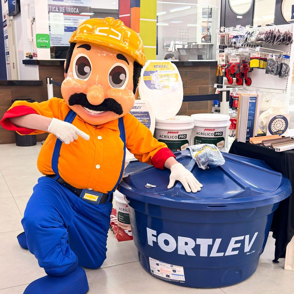 Mascote da Tavinho ao lado de uma caixa d'água Fortlev e de latas de tinta, no salão da loja
